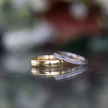 A groom’s wedding ring lies flat on a black glass surface with the accompanying bride's ring resting half on top of it.