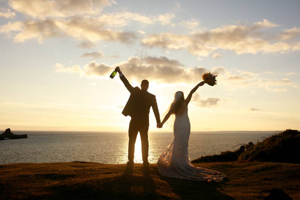 A bride and a groom touch foreheads on their special day. They are sharing a laugh outside with the golden the rays of the warm Welsh summer sun casting over them.