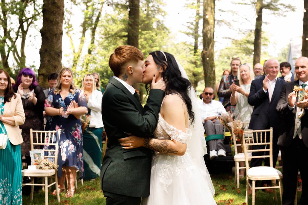 A bride and a groom touch foreheads on their special day. They are sharing a laugh outside with the golden the rays of the warm Welsh summer sun casting over them.